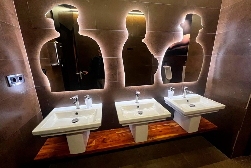 imagen de espejos que tienen formas de personas diferentes  y están colocados encima de cada lavabo